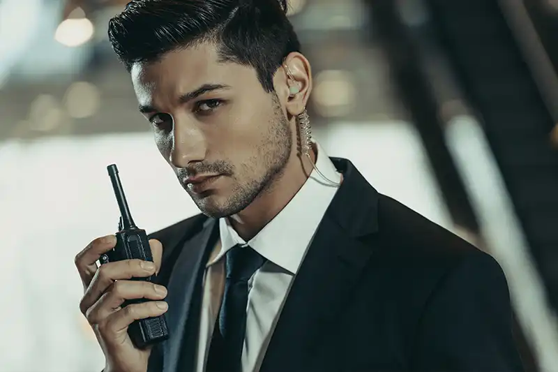 Professional in a suit holding a walkie-talkie, symbolizing executive protection and corporate security training for the Embassy Protector Course.