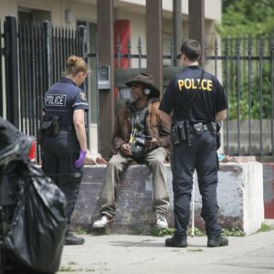 Police officers engaging with an individual experiencing homelessness, illustrating crisis intervention and behavioral health training relevant to law enforcement.